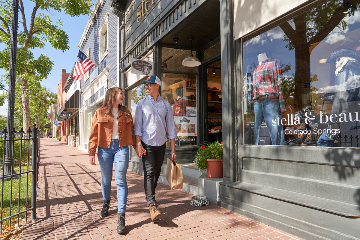 A couple holding hands and walking along a brick sidewalk past local shops in Old Colorado City near Colorado Springs