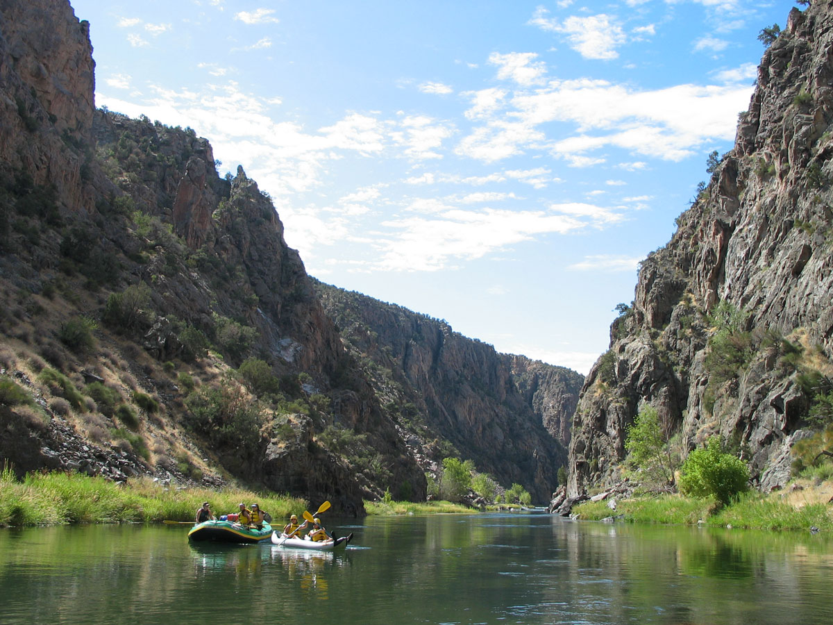 Rafters and kayakers floating on the Gunnison River between steep canyon walls in western Colorado.