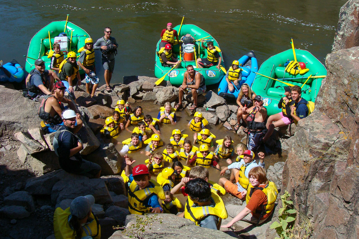 Group of rafters relaxing in Radium Hot Springs along the Upper Colorado River, with rafts pulled up along the shore.