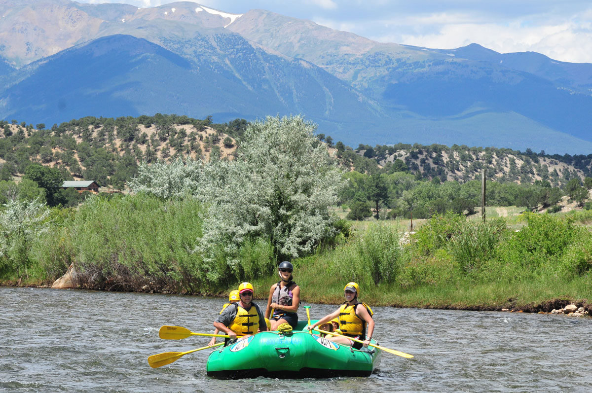 Three rafters float down a calm stretch of Lower Browns Canyon near Salida and Buena Vista with mountains in the background.