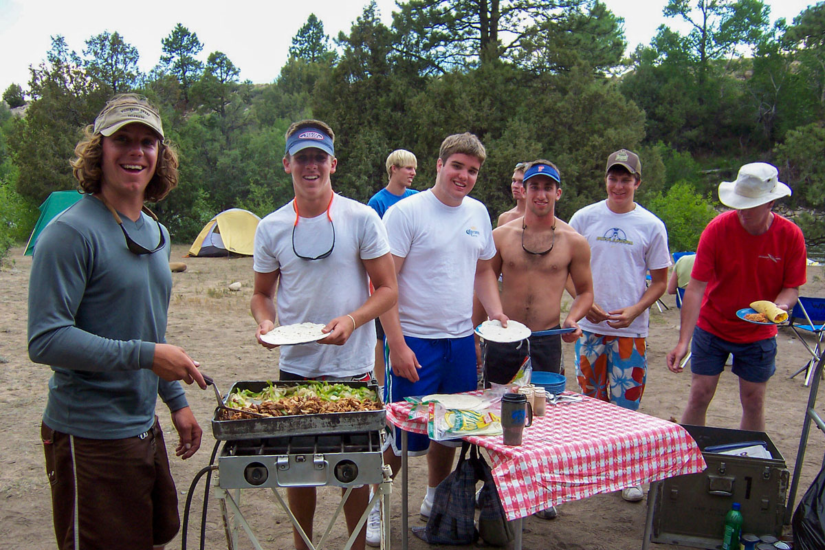 A group of rafters prepare a meal at a riverside campsite during a multi-day trip with Wilderness Aware Rafting.