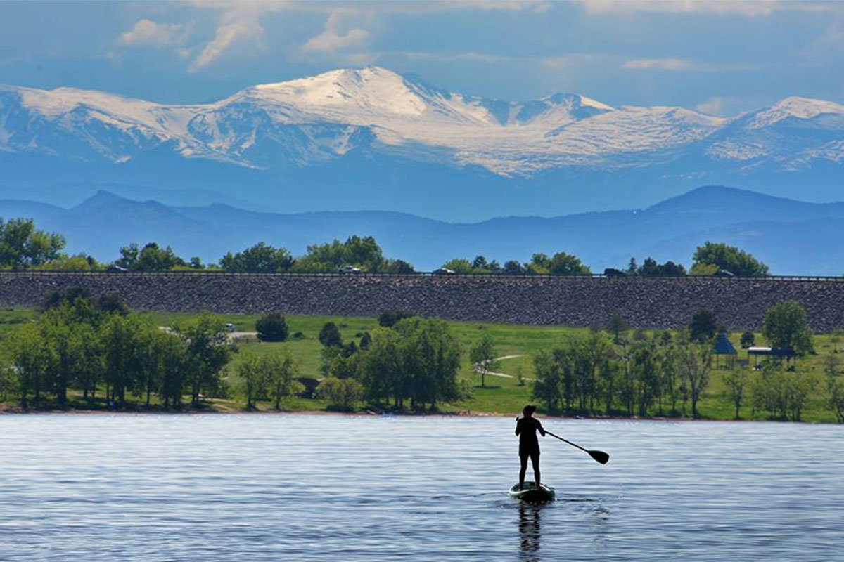 A person paddleboards on a lake with snowcapped mountains in the distance in Aurora, Colorado.