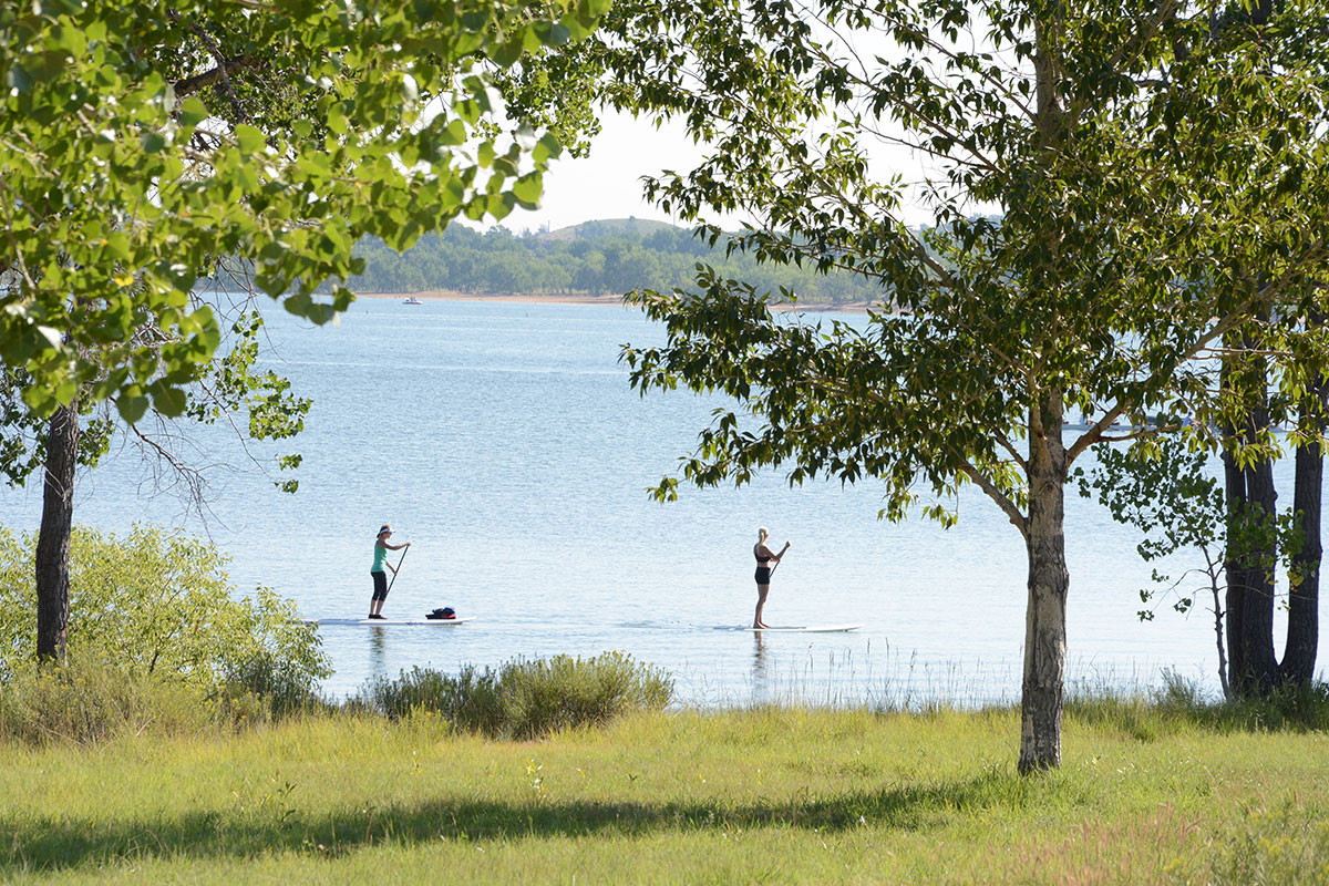 Two people paddleboard on a lake surrounded by trees in Aurora, Colorado