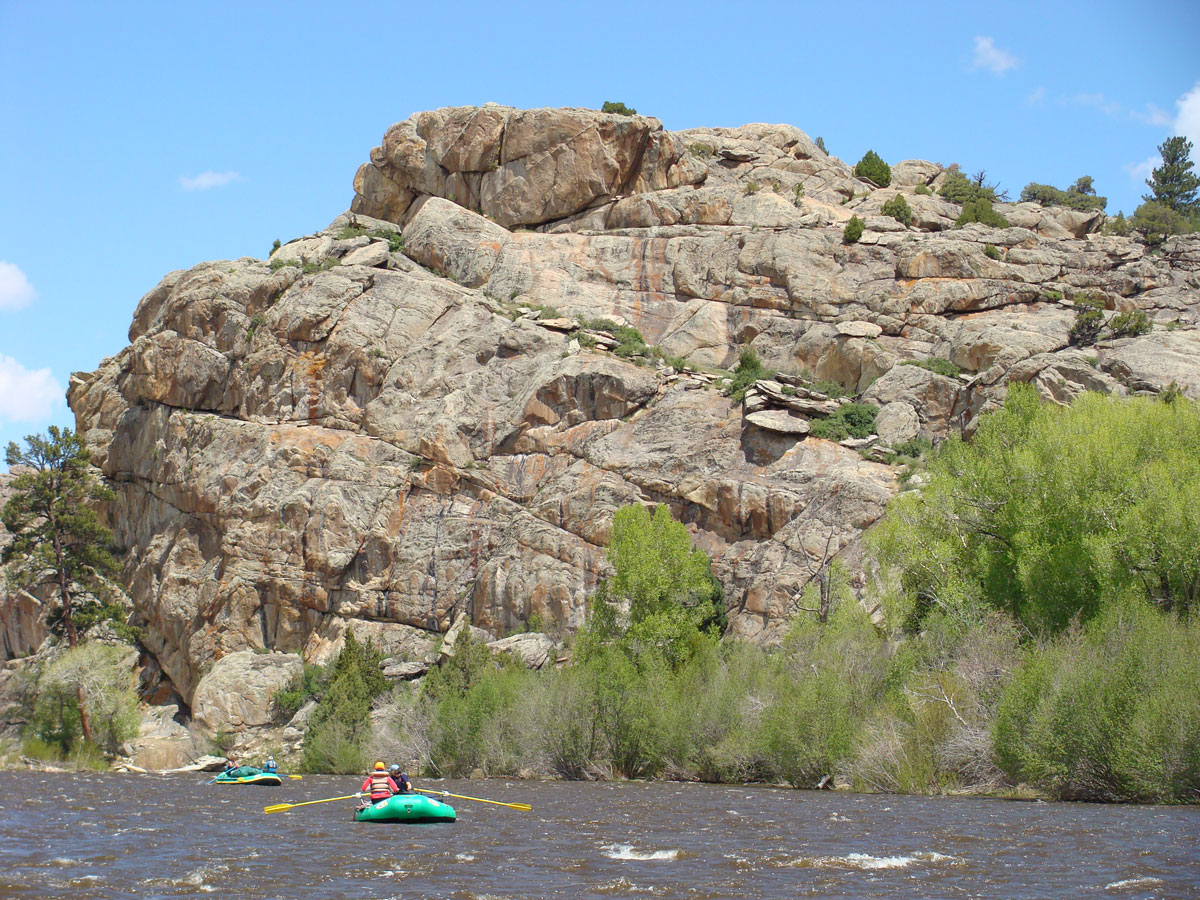 Rafters float along the North Platte River in northern Colorado beside large rock formations and riverside greenery. 