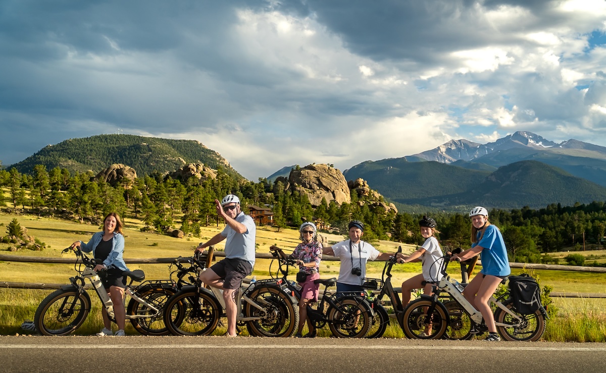Group of e-bike riders posing on a path with mountains in the background in Estes Park, Colorado.