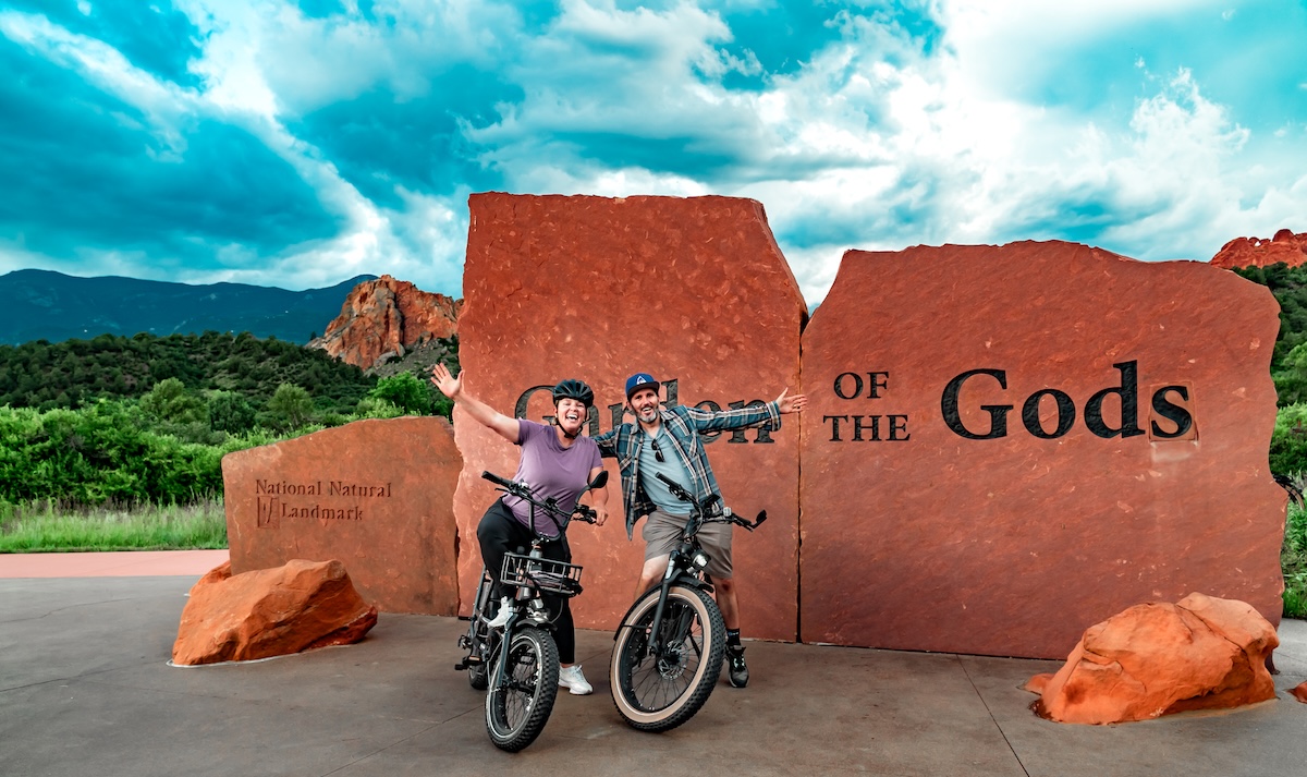 E-bike riders posing in front of the Garden of the Gods entrance sign in Colorado.