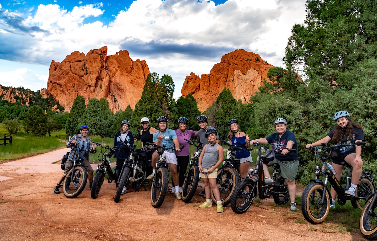 E-bike riders posing at Garden of the Gods with orange rock formations in the background in Colorado.