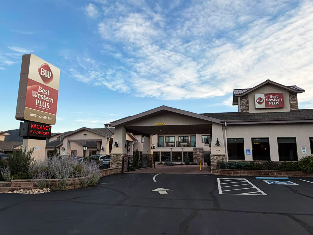 Entrance to the Best Western Plus Silver Saddle Inn with a covered driveway and hotel sign under a blue, cloud-filled sky.