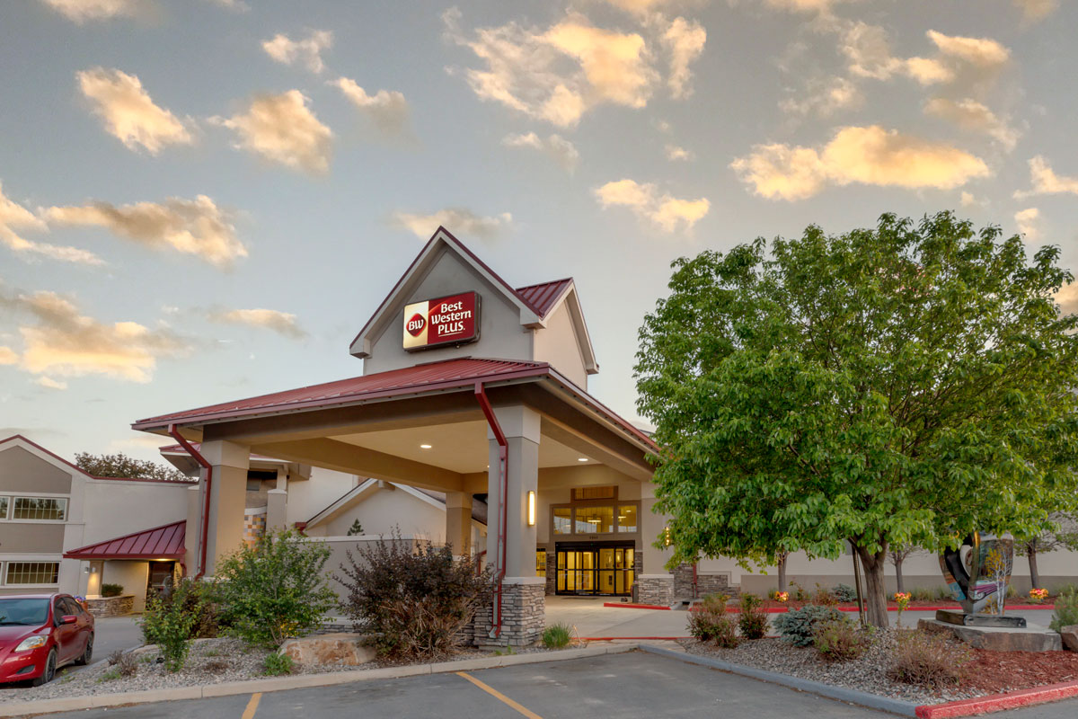 Entrance to the Best Western Plus Loveland Inn with a covered driveway and leafy trees under a partly cloudy sky.