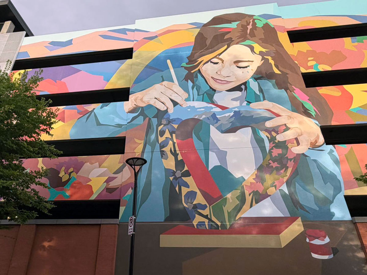 Colorful mural depicting a woman painting a heart-shaped sculpture on the side of a building in Loveland, Colorado.