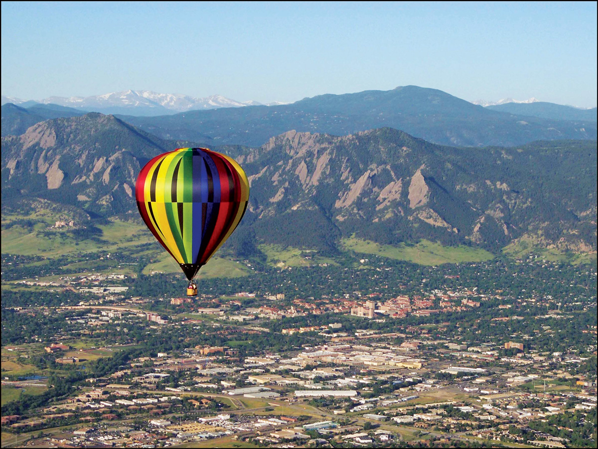 A rainbow-colored hot-air balloon flys over soaring Rocky Mountain views.