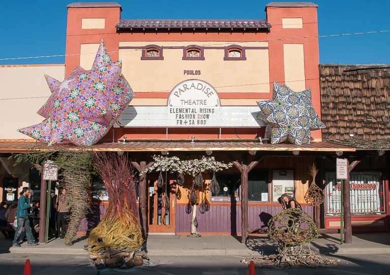 The Paradise Theatre's entrance has two geometric sculptures on top of the roof. People walk past sculptures on the sidewalk.