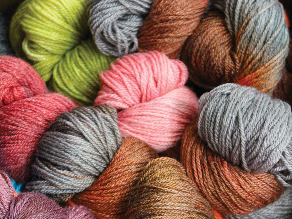 Skeins of dyed yarn are neatly bundled and set together. The colors range from cherry-blossom pinks and apple-green to blue-gray and tie-dye-style brown.