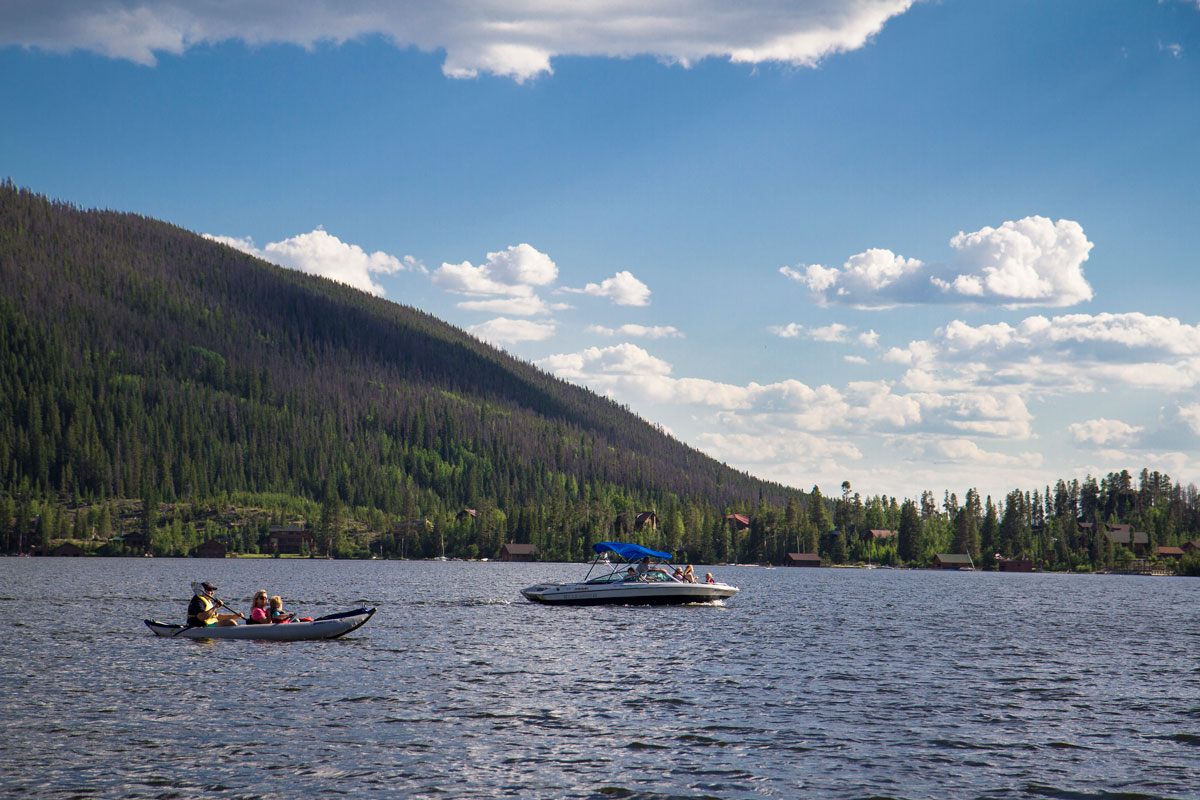 Two kayaks glide along a lake with mountains in the background