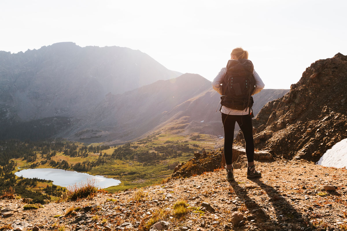 A hiker stands on an overlook as the sun shines over the mountains