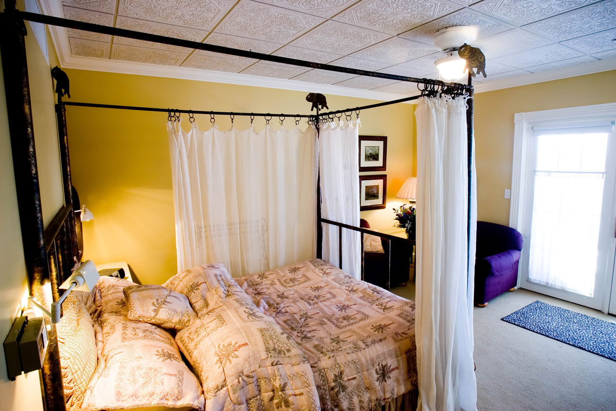 A bed is piled high with pillows and covered with sheets and a comforter, featuring a palm-tree and squares design, in a guest room in Colorado Springs.