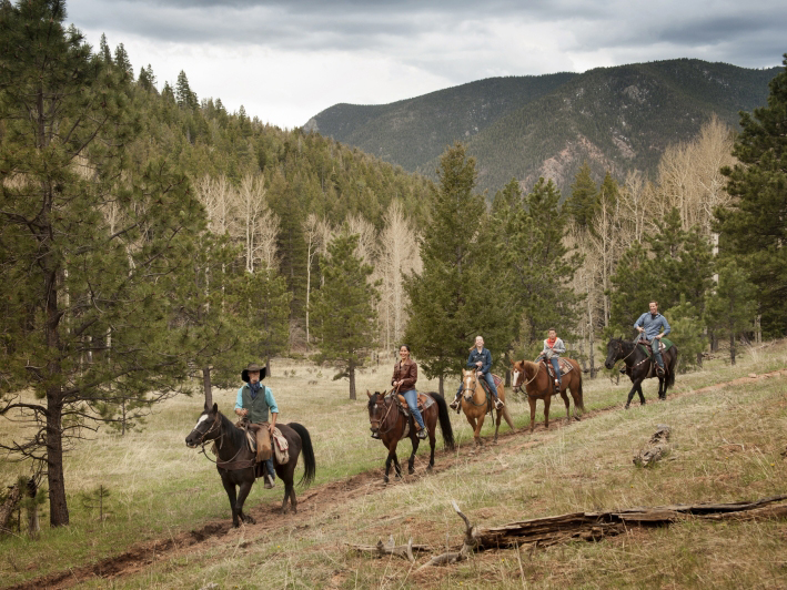 Five riders follow a dirt track along a pine-forest valley floor in the wilds of Colorado.