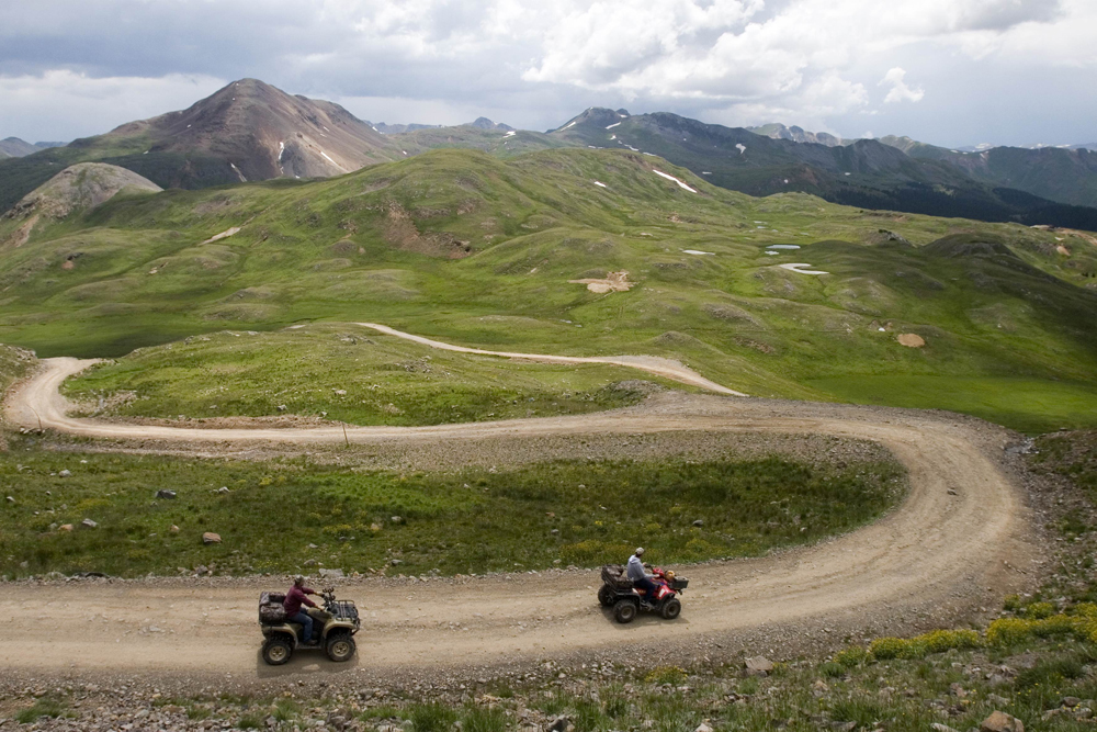 Two people ride ATVs on a rocky trail that winds over rolling hills in Engineer Pass near Ouray, Colorado.
