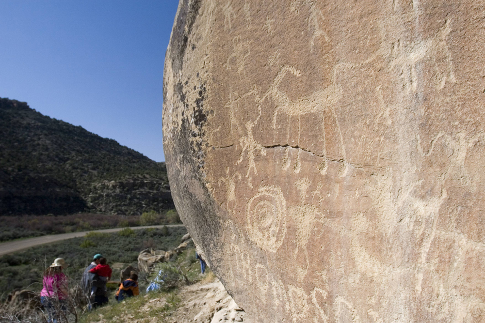 A tour group gazes up, where pictographs are carved into a rock face