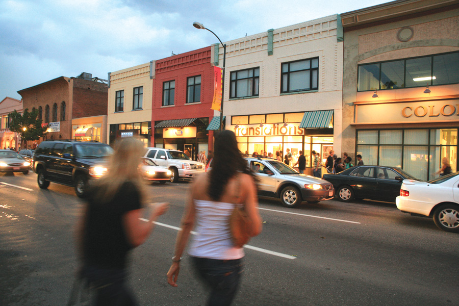 To women cross the street toward a row of galleries with big picture windows glowing with welcoming light