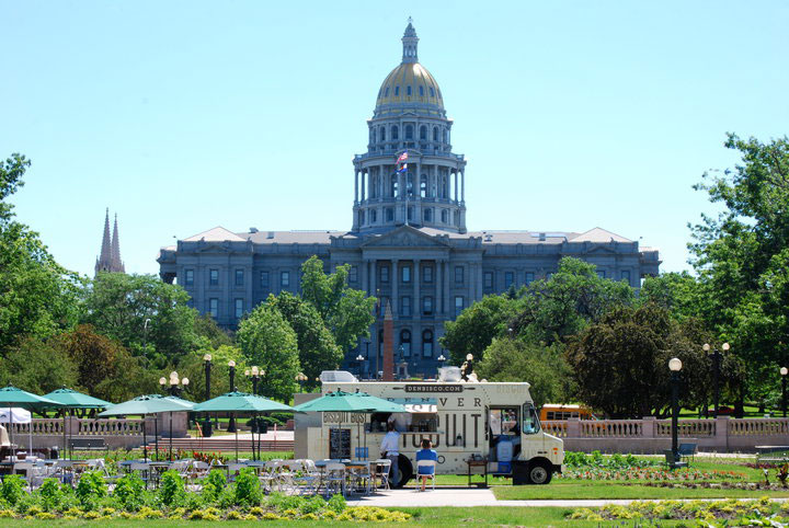 The Denver Biscuit Bus food truck is parked in front of the towering Colorado State Capitol building on a sunny summer day