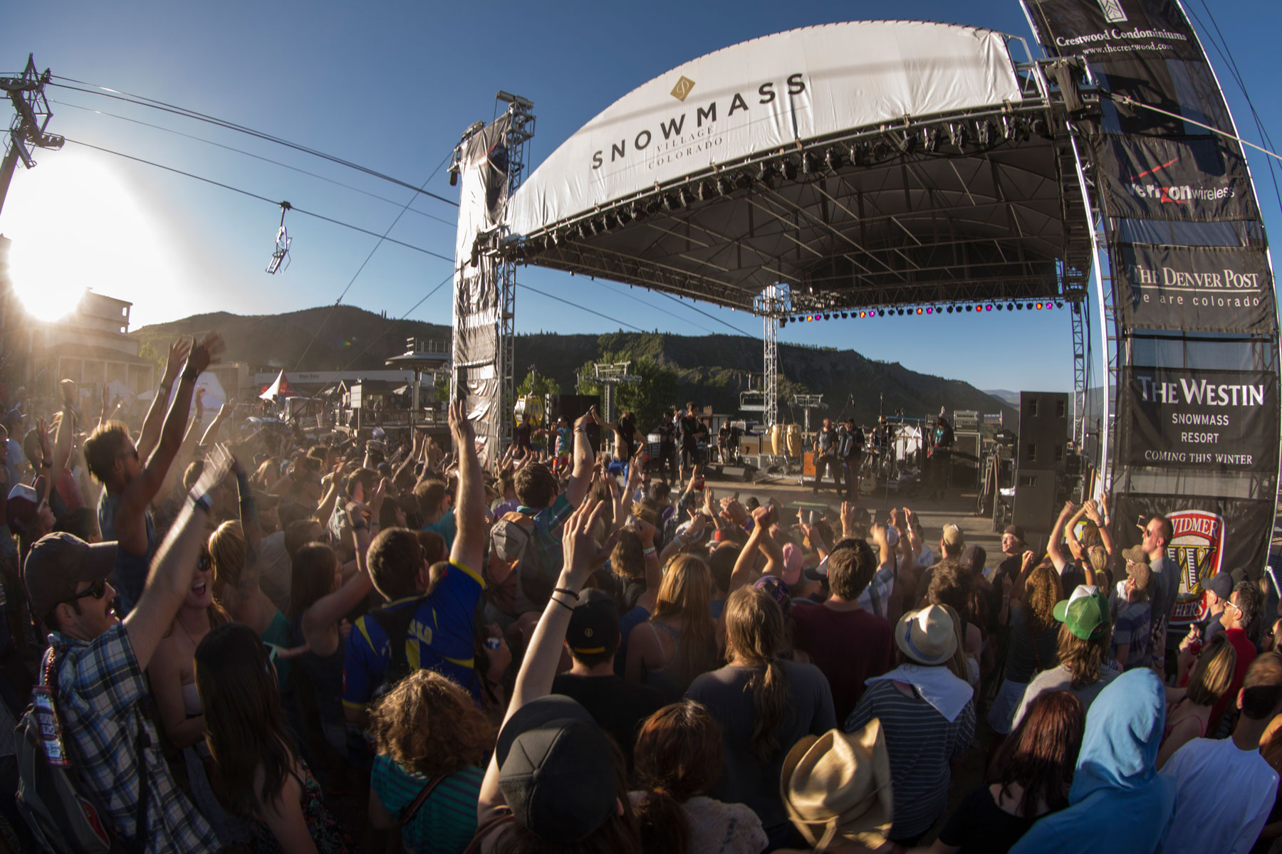 A rambunctious audience cheers and raises its hands for the group performing on a raised stage at the Snowmass Mammoth Fest. 
