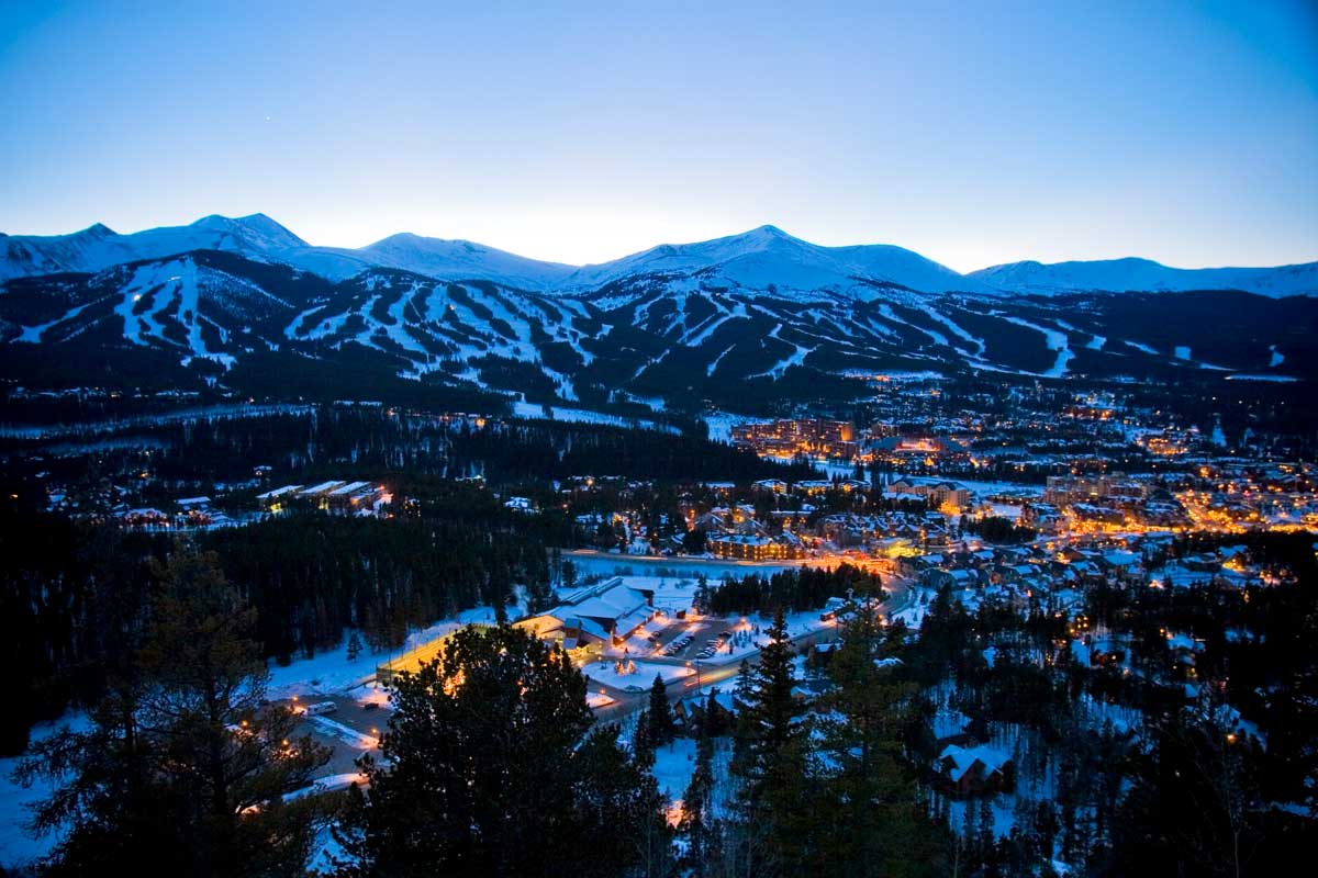 An aerial view of Breckenridge glowing in the dusk light as snow covers the mountain slopes.