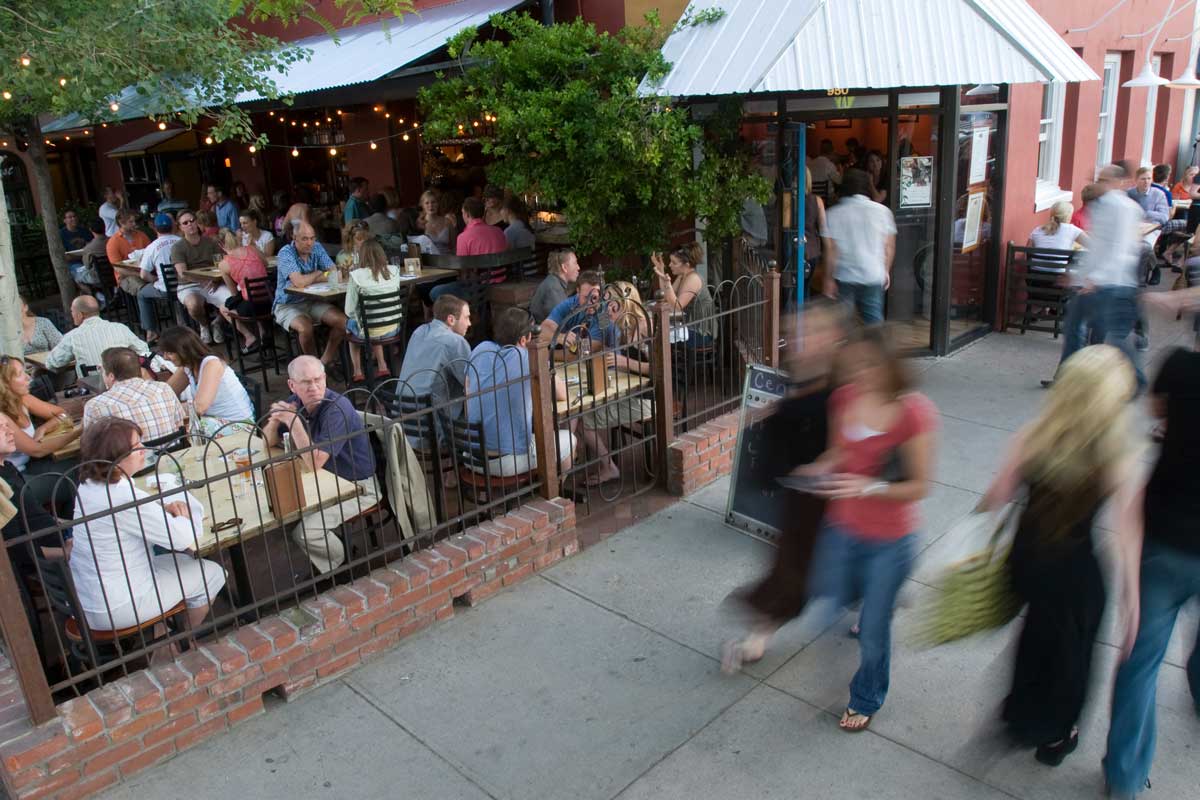 People sit on an outdoor patio as other people walk by on the sidewalk in Old Town Fort Collins.