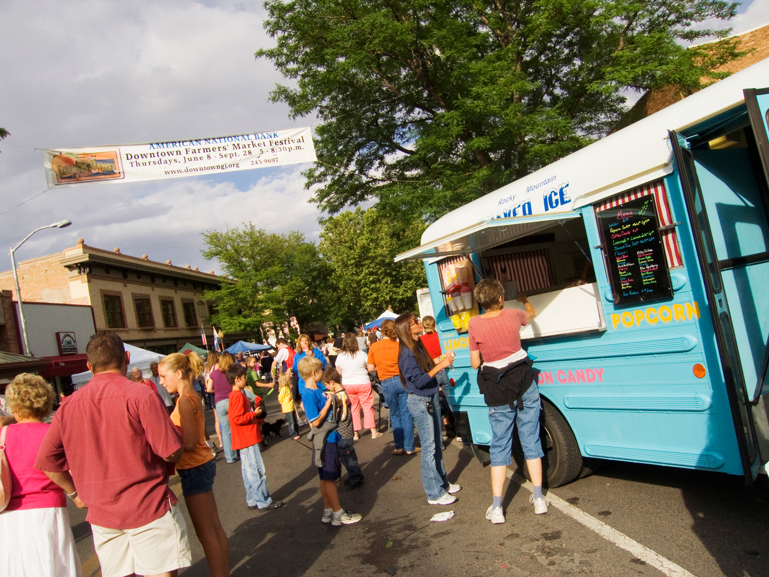 People line up at a blue food truck at weekly summer farmers' market in downtown Grand Junction