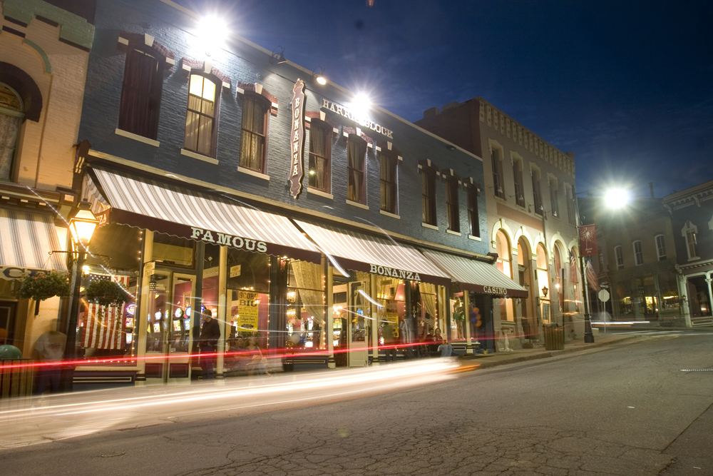 Old-style gaming halls — brick buildings painted green — line the street; lights glow from within and without