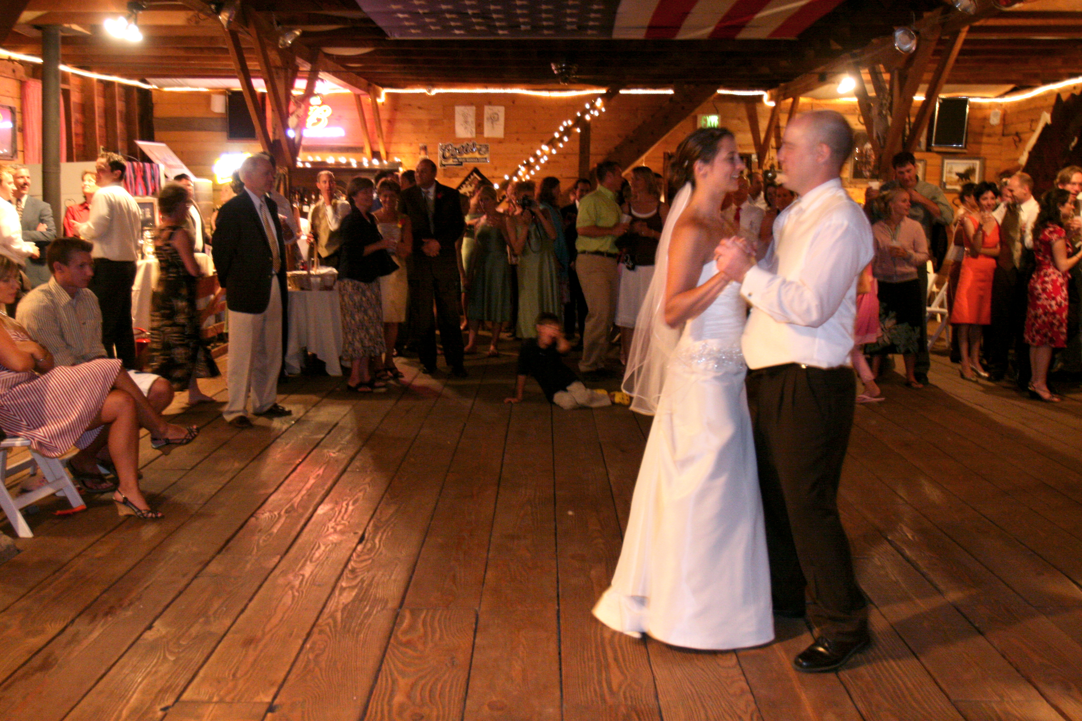 A bride and groom dance closely together in a barn in Colorado. They are alone on the dance floor with a crowd of family and friends watching from the sidelines.