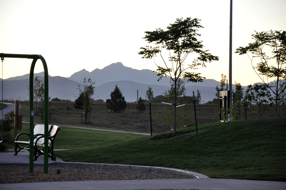 A sunset view of the Front Range mountains from a park in Erie. Recently planted trees sit near a bench with a golden sky.