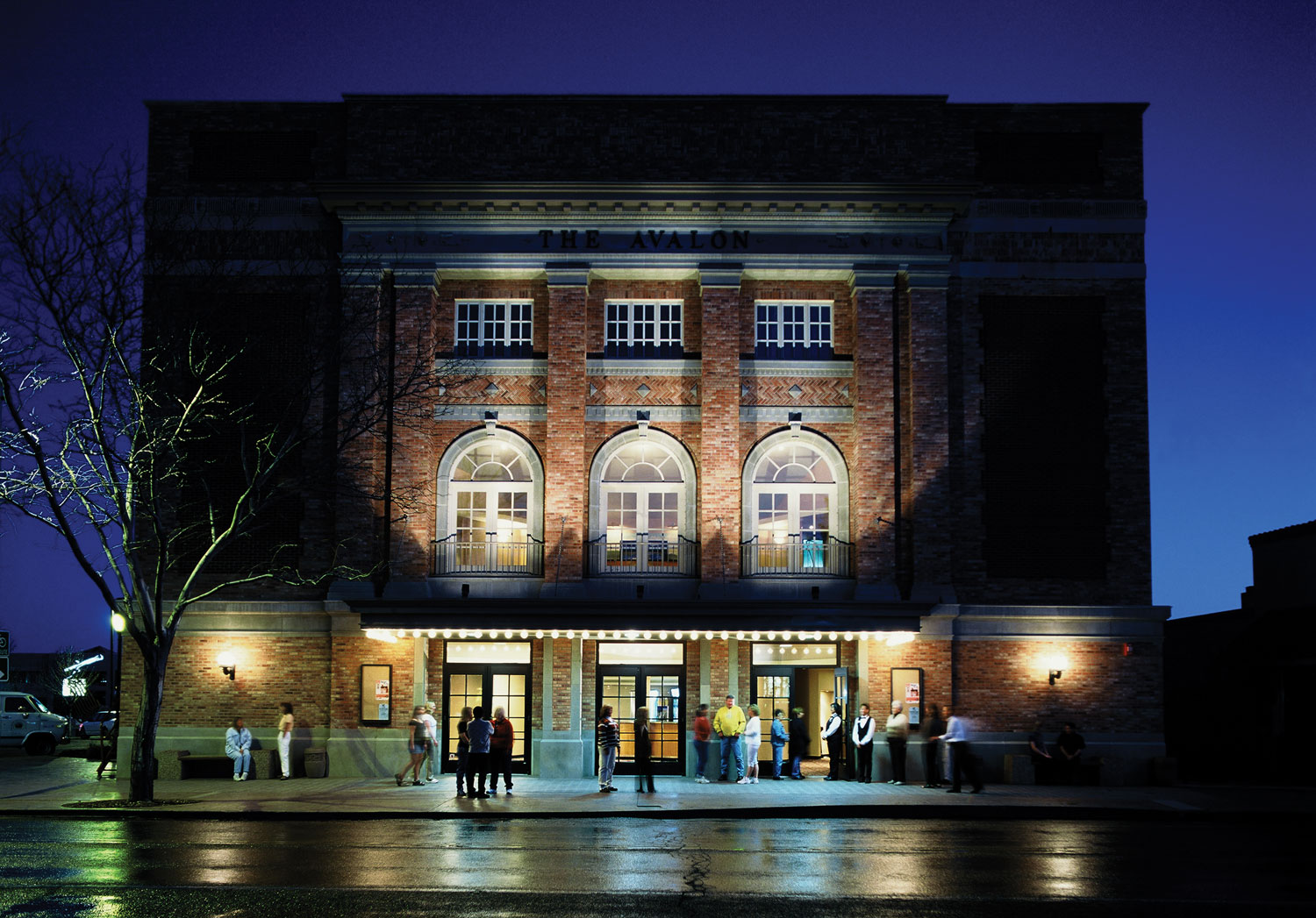 People mingle outside a brick building in Grand Junction. The building is lit up with lights and stands out against the night sky.