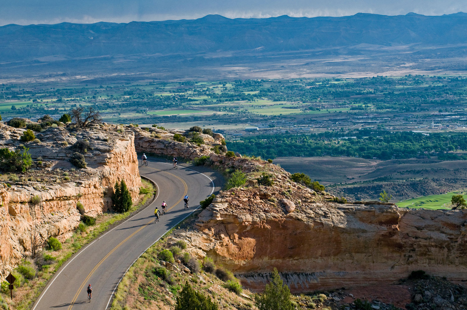 Bikers ride along a mountain road with a beautiful valley spread out below