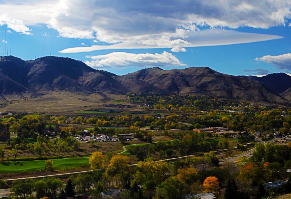 An aerial view of the valley of Golden in the summer with green grass, green trees and a blue sky with white clouds. The foothills of the Rocky Mountains are in the distance.