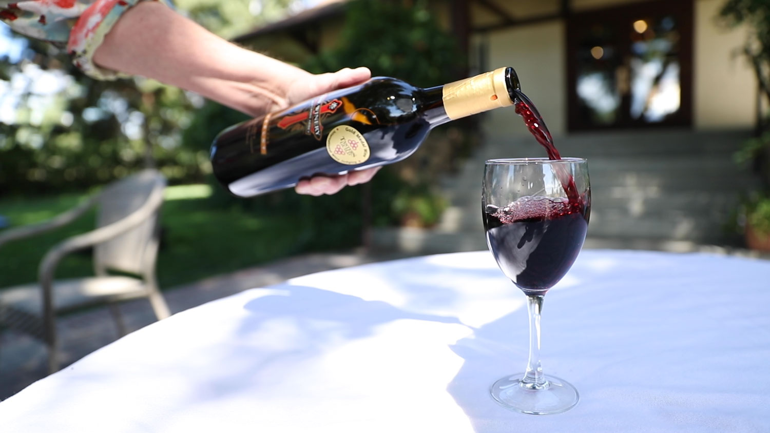 A person pours a bottle of red wine into a stemmed glass on the outdoor patio at the Winery at Holy Cross Abbey in Cañon City, Colorado.
