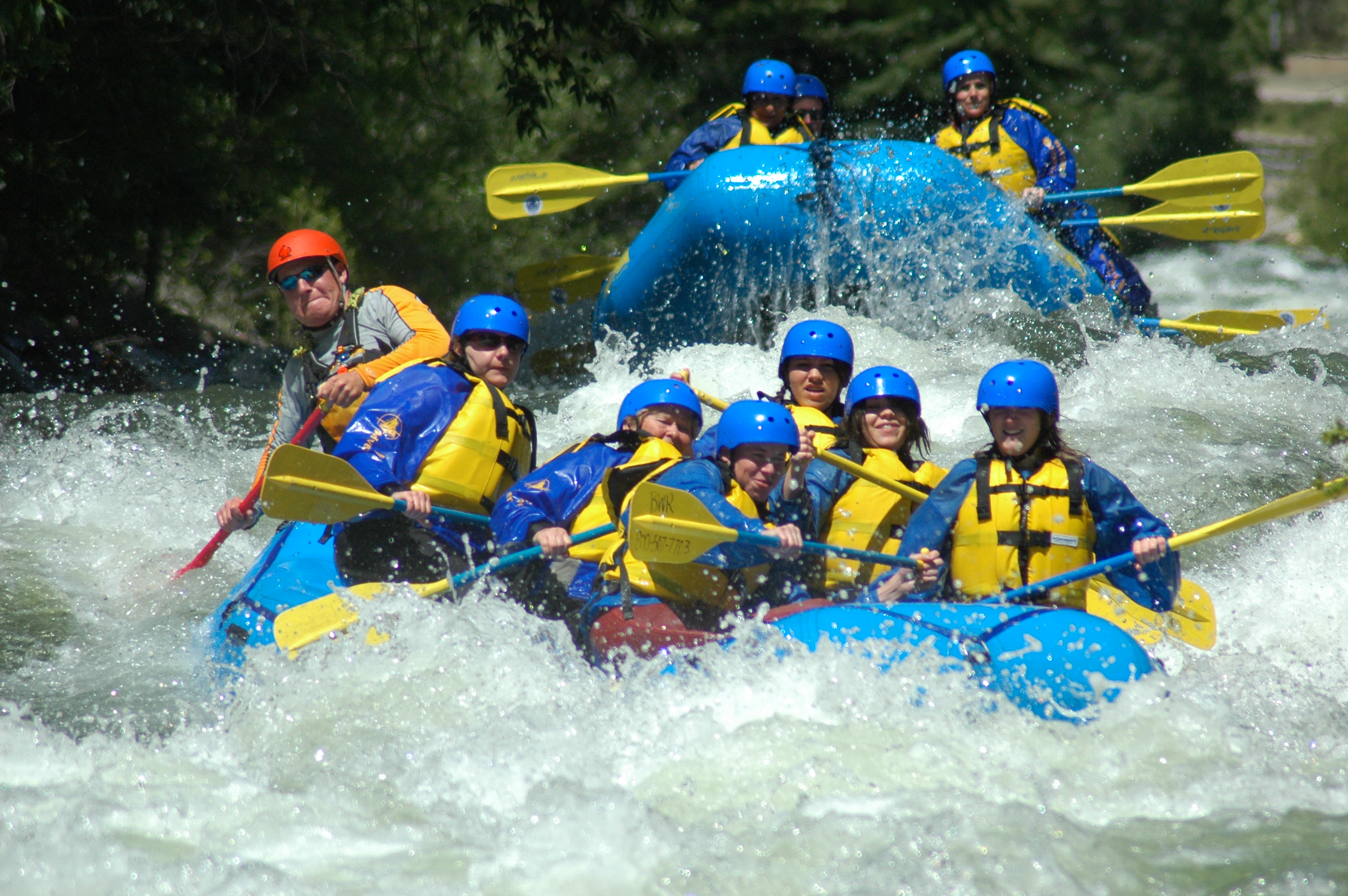 Two blue inflatable rafts are filled with riders push through whitewater rapids on Clear Creek with Colorado Adventure Center guides.