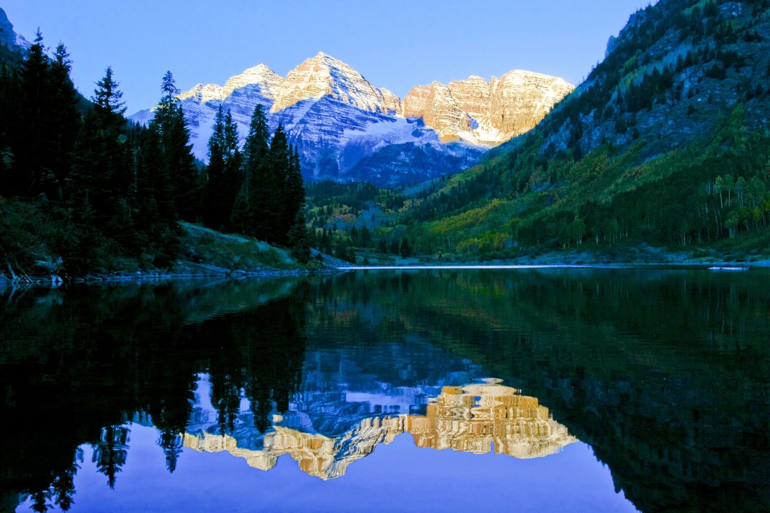 A snow-capped mountain view is reflected in a glassy lake