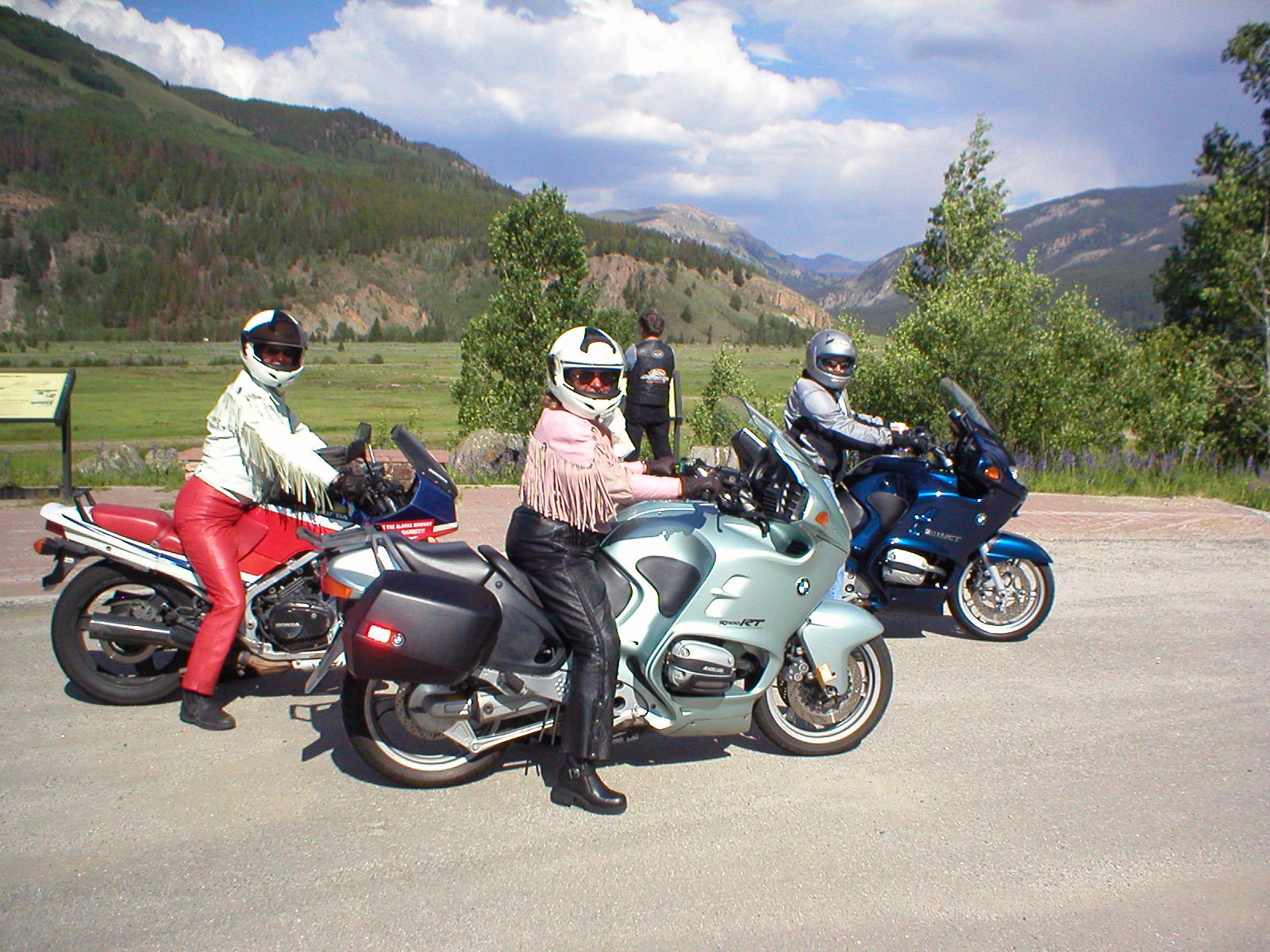 A group of riders, two in fringe-lined leather jackets and two non-leather jackets, make a scenic stop near Vail, Colorado.