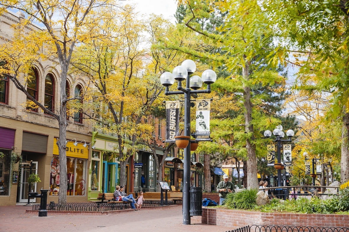 A line of shops on Pearl Street in Boulder with a green tree and street lamp in the foreground