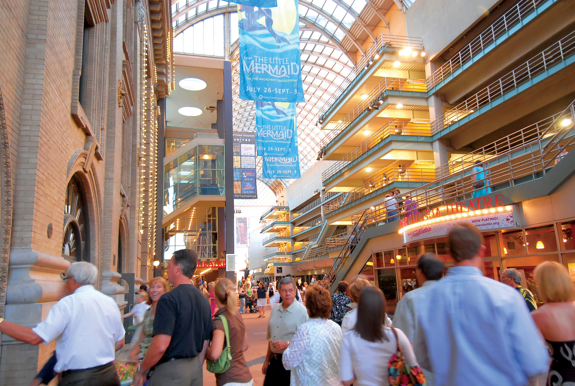 People roam the multiple floors of a mall-like complex in Denver. Flags nearby highlight a showing of The Little Mermaid.