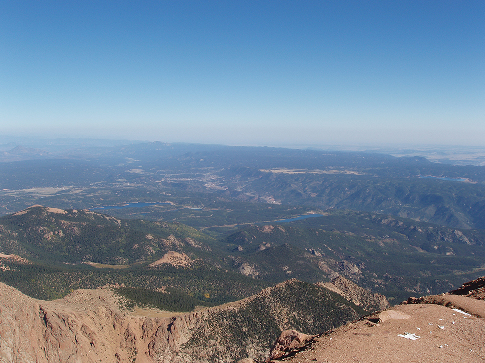 A view from high up in Pikes Peak shows a rugged valley with dark-green trees below.