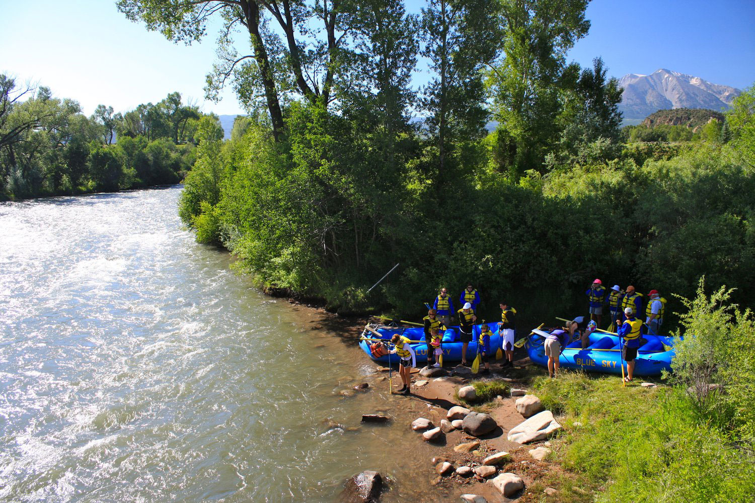 Two rafts are pulled up on a river bank on a rafting tour on a sunny day