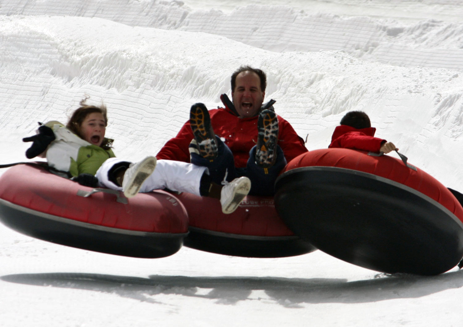 Three snow tubers get air atop red snow tubes on a snowy field.