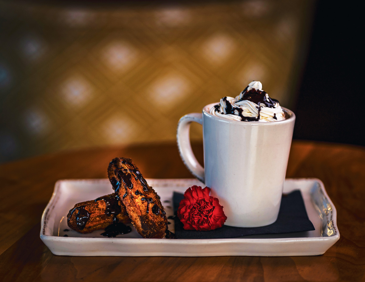 A plate of churros and a hot chocolate with whipped cream, both drizzled with chocolate