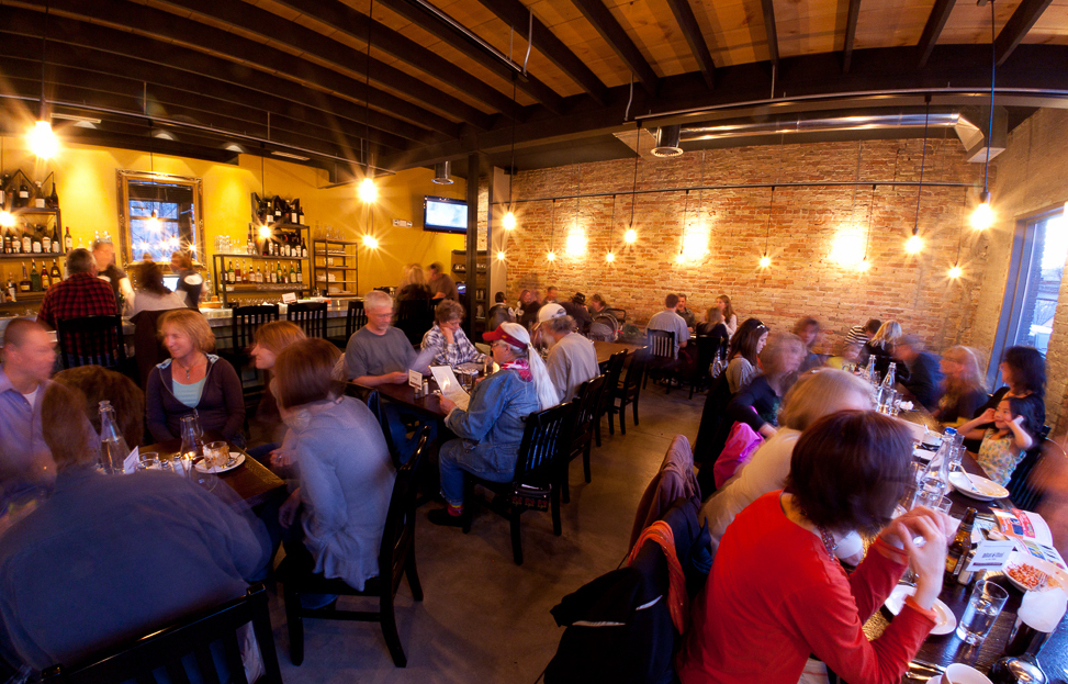 Diners sit at tables in a dining room. Above them, sparkly lights give the room a warm glow.