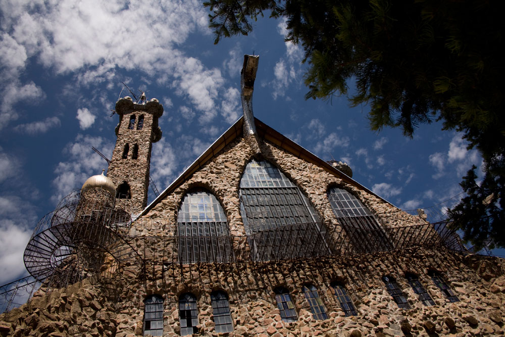 From the ground looking up, Bishop's Castle, a stone building with lots of wrought-iron details sits under a blue sky. 