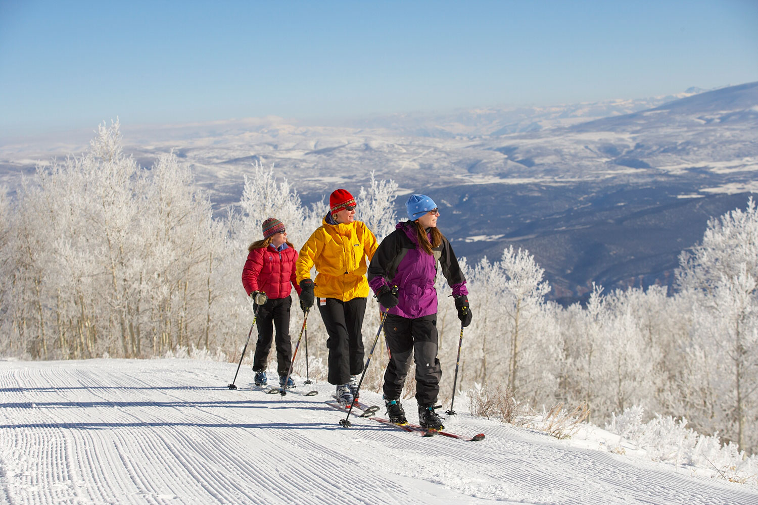 Three people trek across a groomed cross-country skiing trail near Glenwood Springs with snowcapped mountains in the background