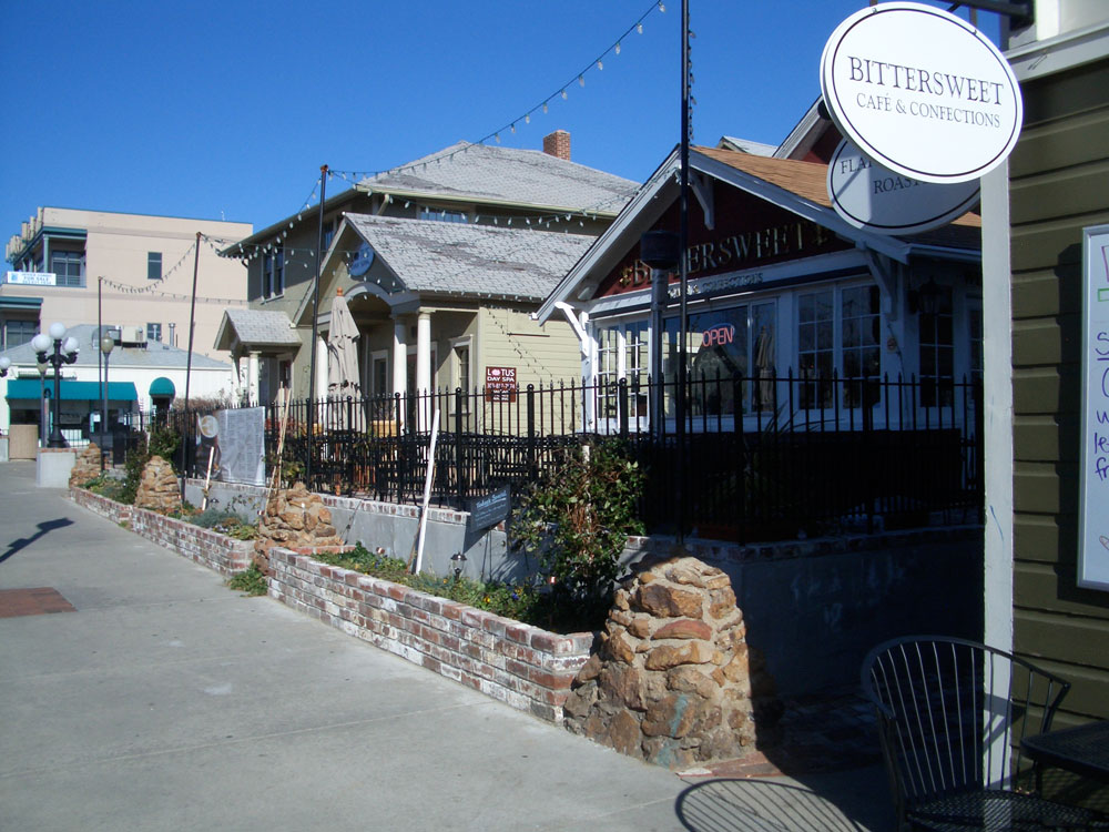 Houses that have been turned into shops and restaurants with twinkle light strung between them sit on the right side of the image with a low brick wall along the sidewalk that's on the left.
