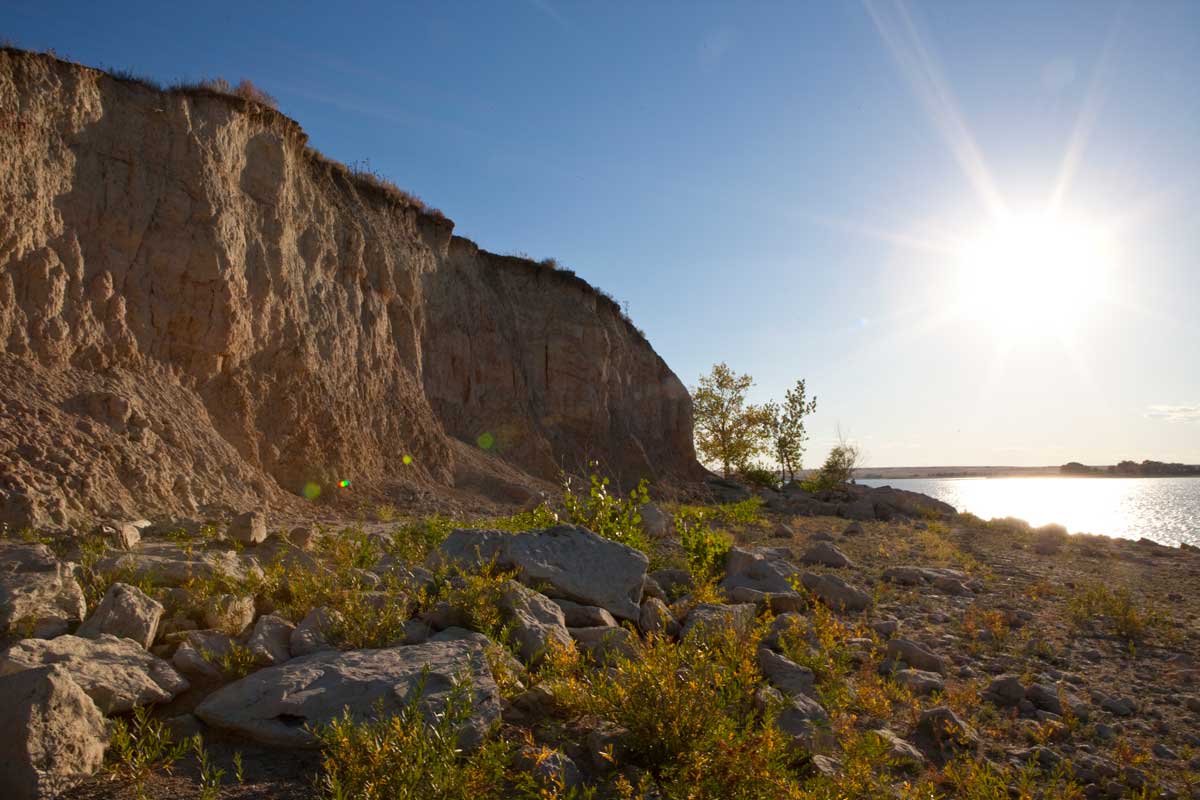 The rocky shore of the lake at North Sterling State Park sits under a sunny blue sky.
